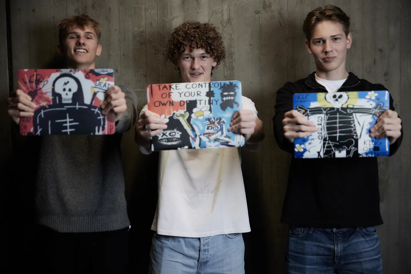 Tre unge med KUUNIG-artwork på deres laptopcovers