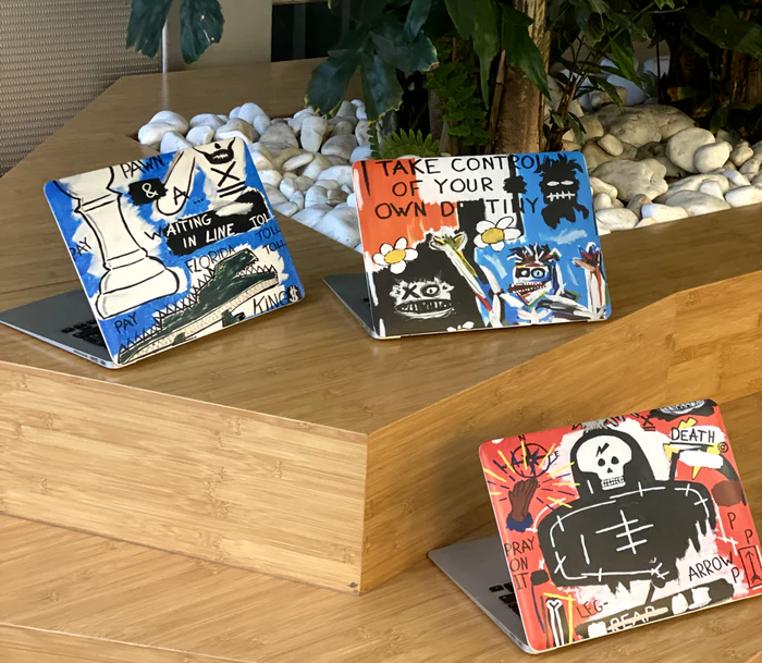 Tre malede laptopcovers fra KUUNIG på en bænk